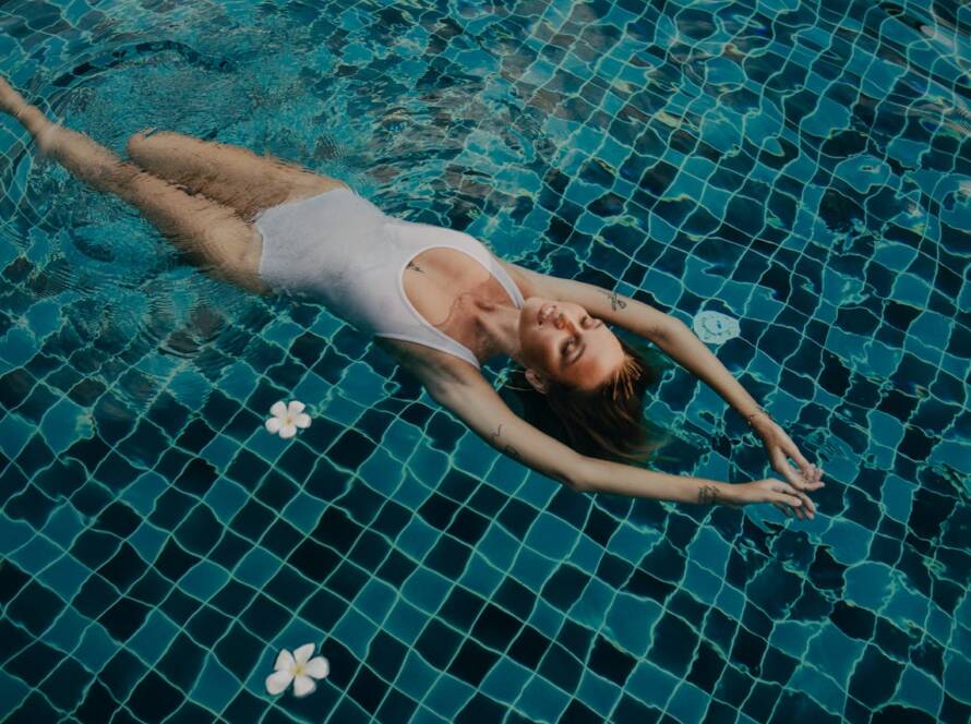 A woman in a white swimsuit floating peacefully in a Bali pool.